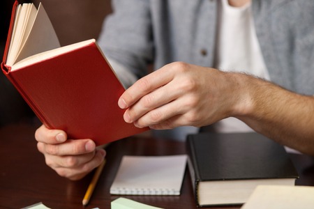 Close up of hands of a student reading the book at the library. The man is sitting at the table and holding the bookの写真素材
