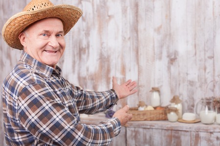 Happy old man is showing dairy products on the table and smiling. He is standing and pointing his arms sidewaysの写真素材