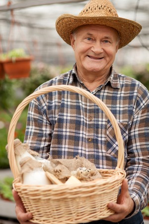 Professional old farmer is presenting a basket of milk and eggs. The man is standing in his garden and smiling. He is looking at camera happilyの写真素材