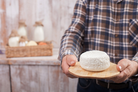 Close up of hands of old farmer holding a stand with cheese. The man is standing. A basket of dairy...