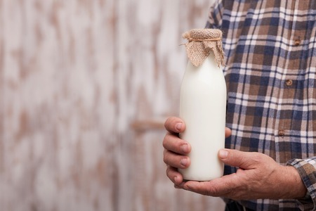 Close up of hands of old man holding a bottle of milk. The farmer is standing. Copy space in left sideの写真素材