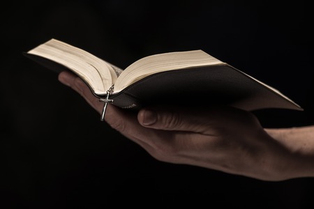 Close up of arms of young woman reading a bible. She is holding an open book. Isolated on black backgroundの写真素材