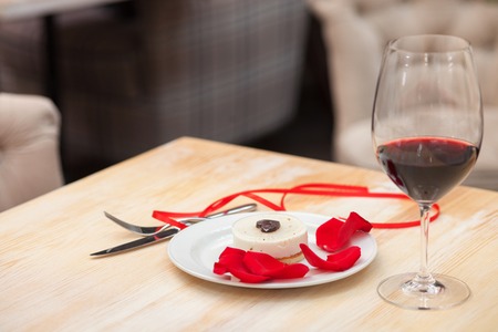 Close up of Valentine diner on the table in restaurant. Glass of red wine, tasty cake and rose petalsの写真素材