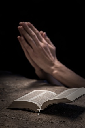 Close up of hands of young woman praying near the Bible. She is clapping her arms together