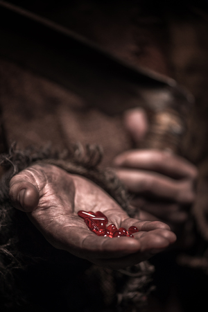 Close up of hands of grim Reaper holding red narcotic pills and scytheの写真素材