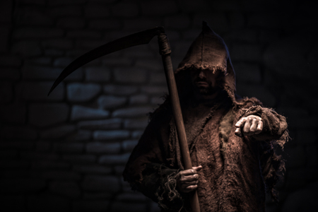 Frightful epitome of death is standing with a scythe. The man is pointing his finger forward with treats. He is very serious. Copy space in left sideの写真素材