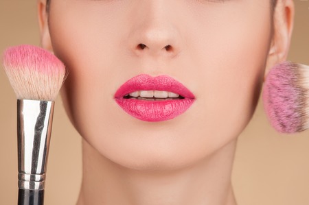 Close up of lower part of the face of young woman. She is getting blush on her cheeks with two brushesの写真素材