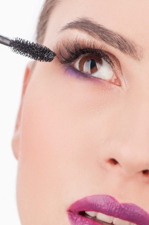 Close up of attractive young woman getting make-up. The beautician is putting on mascara on her eyelash. The girl is looking up with desireの写真素材