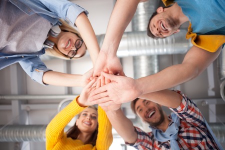 Cheerful creative team is joining hands with joy. They are working in cooperation with joy. The men...