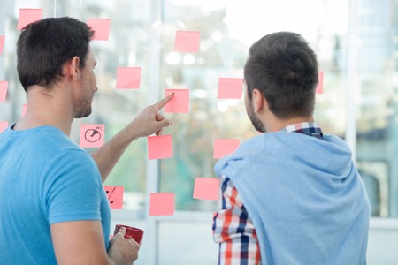 Skillful young colleagues are working together in office. They are standing and looking at the...