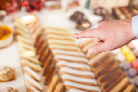 Close up of male hand of customer buying food in bakery. He is pointing finger at the cakeの写真素材