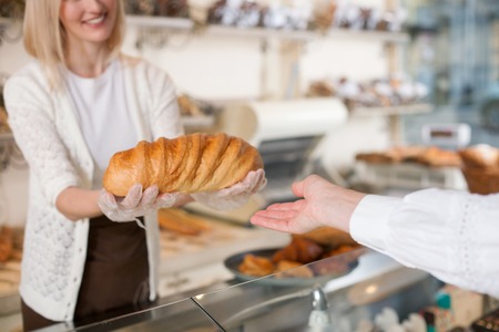 Close up of pretty young saleswoman giving the bread to woman. She is standing and smilingの写真素材
