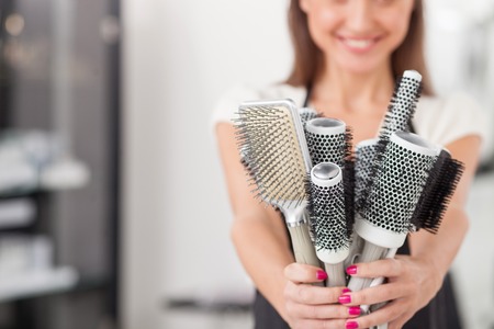 Close up of pretty young hairdresser holding many combs and showing it to the camera. The woman is standing and smiling. Copy space in left sideの写真素材