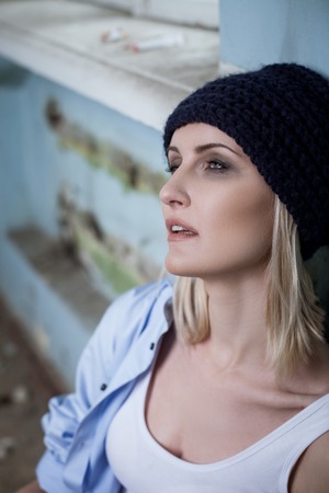 Stressful drug addict is taking heroin. She is sitting and leaning on the wall. The woman is looking...
