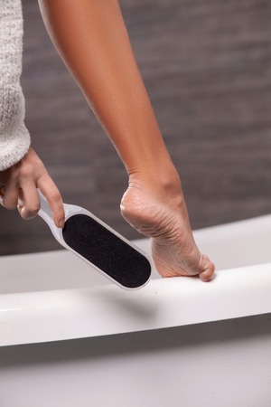 Close up of female leg standing on the bath. The girl is scrubbing her foot with the toolの写真素材