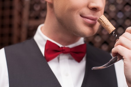 Close up of professional wine waiter examining smell of wine cork. He is standing and smilingの写真素材