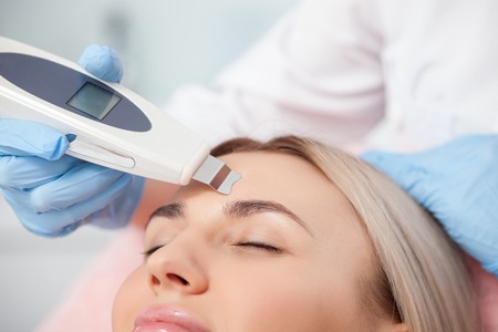 Close up of hands of cosmetologist undergoing skin treatment with the equipment. The young woman...