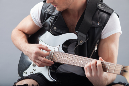 Close up of arms of cheerful musician playing guitar with pleasure. The man is sitting and plucking the strings.の写真素材