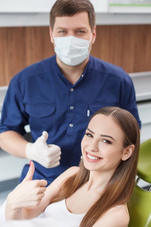 Attractive dental doctor and the woman are giving thumbs up with joy. The lady is sitting and smiling. She likes the work of doctorの写真素材