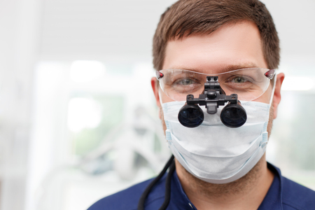Cheerful dentist is standing and looking at the camera with joy. He is wearing medical eyewear and a mask. Copy space in left sideの写真素材