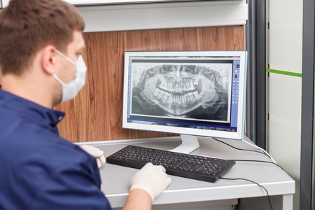 Successful dental doctor is using a computer for analyzing x-ray of human teeth. He is looking at...