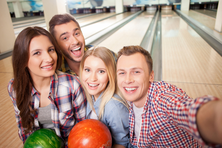 Portrait of friendly bowling team making selfie together. They are standing and laughing. The women are holding ballsの写真素材