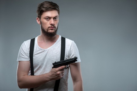 Handsome guy is holding gun in his hand. He is looking menacingly and seriously at the camera....