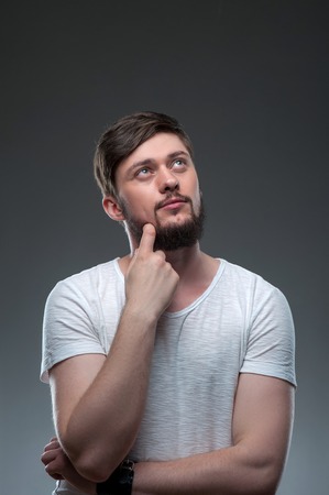 Handsome man is looking up dreamingly. He is touching his beard with his finger. The man is pensive...