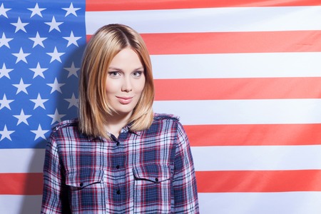 Waist up portrait of beautiful woman standing with USA flag on the background. She is smiling and looking at the camera with happiness. Copy space in right sideの写真素材