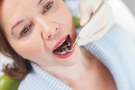 Close up of hands of skillful dentist examining female teeth with a small mirror. The woman is...