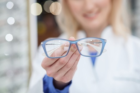 I advise you to buy these eyeglasses. Skillful optician is holding spectacles and smiling. Focus on the eyewearの写真素材