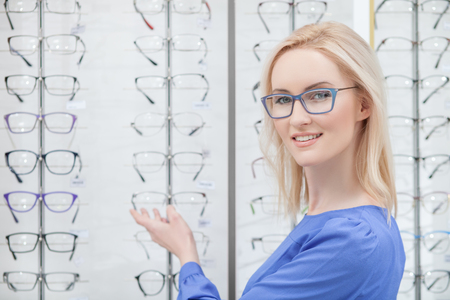 Look at this wonderful selection of spectacles. Waist up portrait of attractive young woman standing in shop and pointing arm at glasses. She is smilingの写真素材