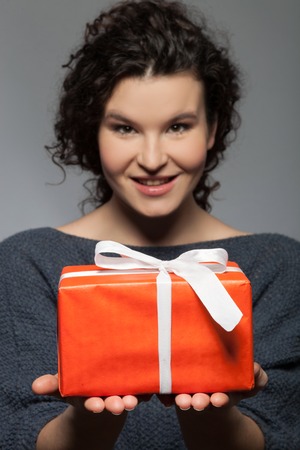 I have a present for you. Portrait of cute woman holding a box and giving it to the camera. She is standing and smiling. Isolatedの写真素材