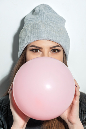 Waist up portrait of attractive girl blowing up a balloon. She is standing and looking at camera with joy. Isolatedの写真素材