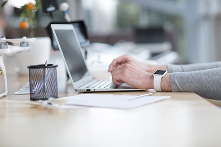 Close up of male hands using a notebook. The man is sitting at the table near the drone. There is a smart watch on his wristの写真素材
