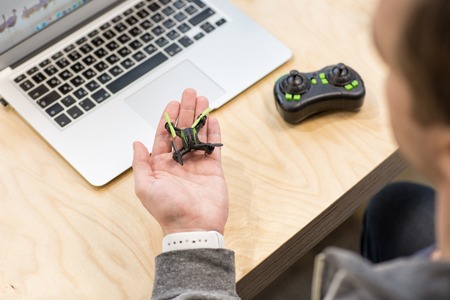Skillful male freelancer is holding a little projected quadrocopter in his hand. The man is sitting...