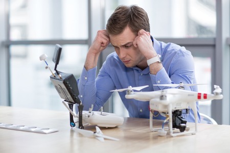Portrait of skillful quadrocopter maker projecting a drone with frustration. He is sitting at the...