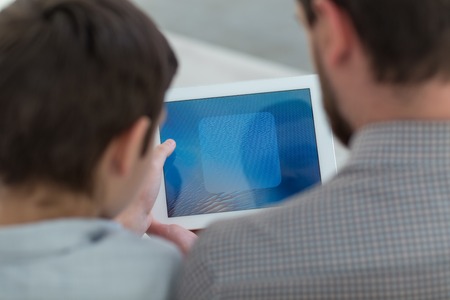 Close up of cheerful father and son using a tablet. Focus on their backs and device