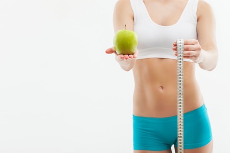 Eat fruits and be slim. Close up of fit body of young female athlete holding an apple and tape-measure. Isolated and copy space in left sideの写真素材