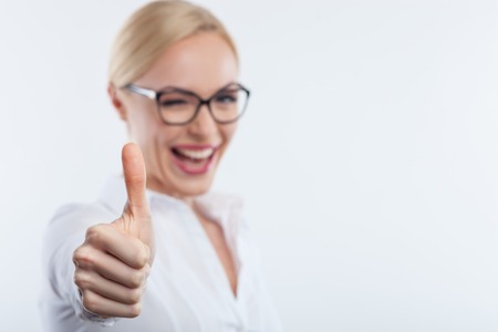 Portrait of beautiful young businesswoman giving thumb up. She is winking and laughing. Isolated and copy space in right sideの写真素材