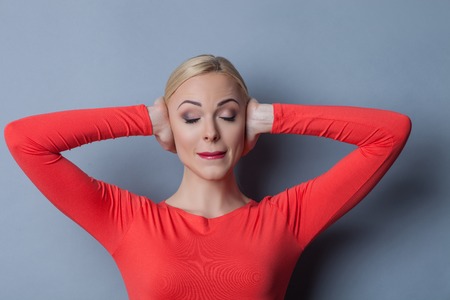 Frustrated girl has a terrible headache. She is covering her ears and crying from migraine. The lady is standing on grey backgroundの写真素材