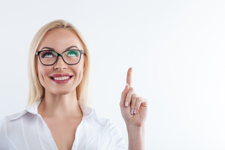Waist up portrait of beautiful young woman raising finger and looking up pensively. She is smiling. Isolated and copy space in right sideの写真素材