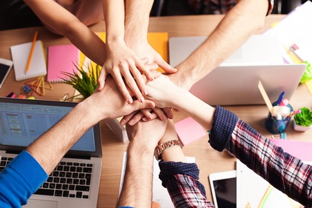 Close up of human arms. Cheerful young colleagues are joining their hands together over the deskの写真素材