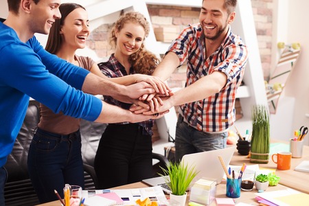 Cute young colleagues are joining their arms together. They are standing and smilingの写真素材