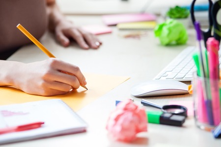 Close up of hands of young businesswoman making some notes on paper.  She is sitting at the desk in officeの写真素材