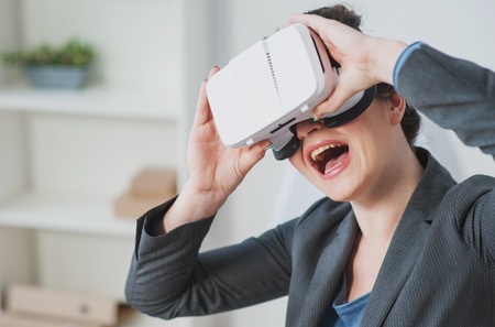 Beautiful woman is entertaining herself with a virtual reality device. She is laughingの写真素材