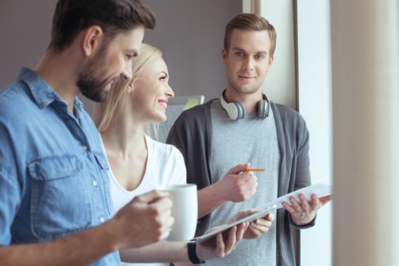Cheerful three colleagues are discussing new project. They are standing and smiling. Woman is...
