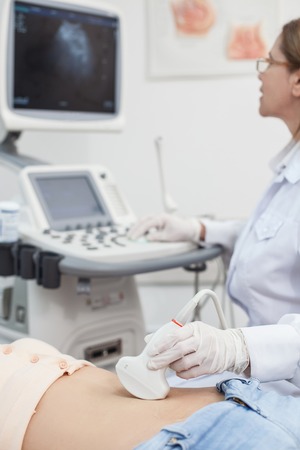 Professional gynecologist is moving ultrasound transducer on human belly. Woman is lying. Doctor is looking at the monitor with concentrationの写真素材