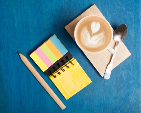 Top view close-up of cup of coffee with spoon, writing-pad, pencil on desk