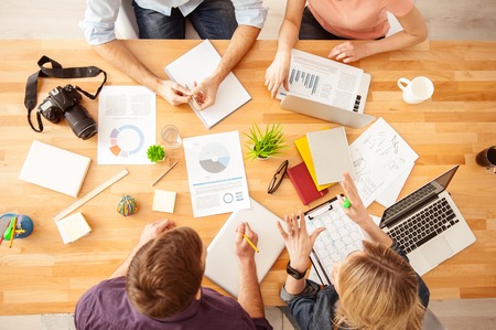 Top view of cheerful young colleagues sitting at the table and talking with concentration